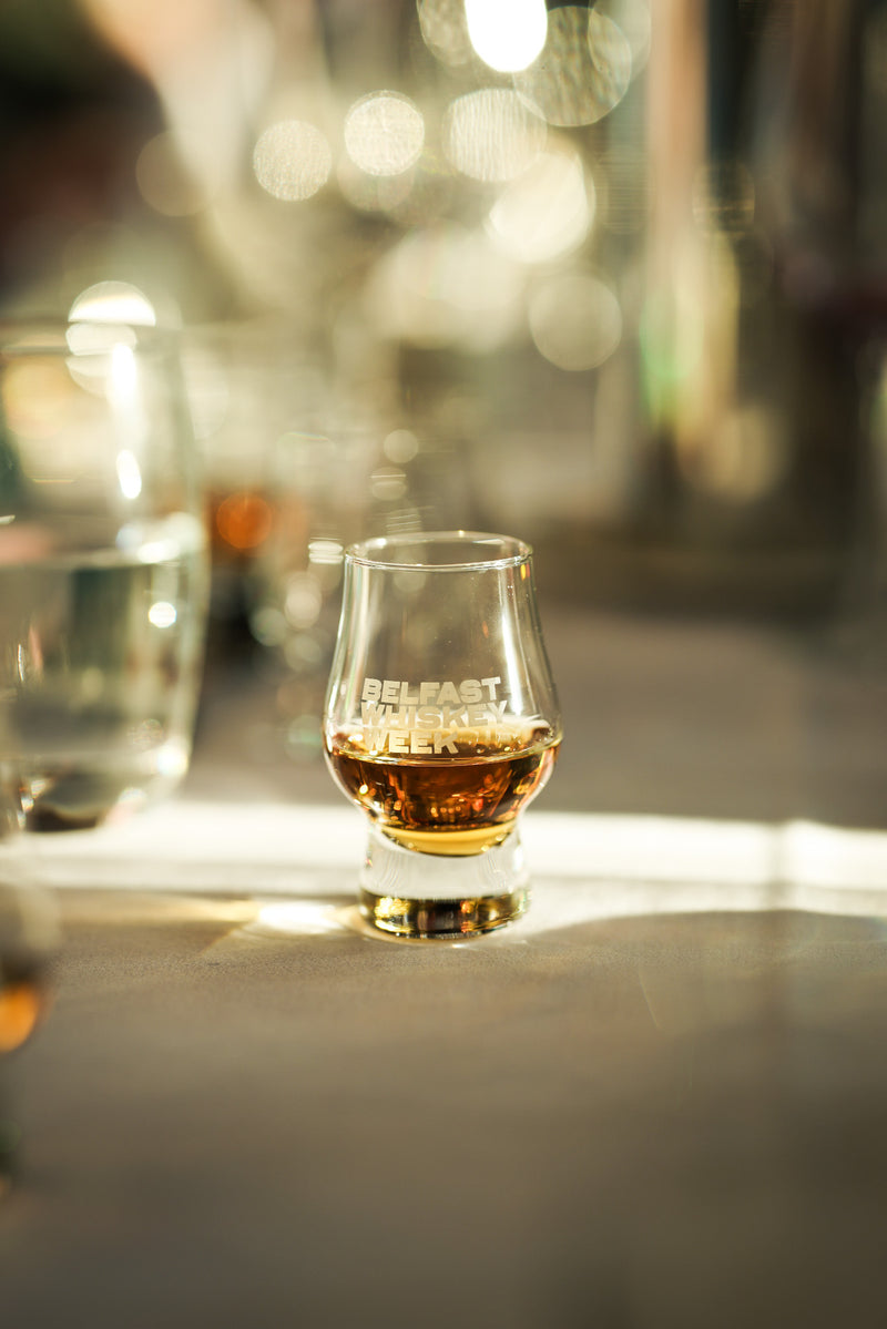 Belfast Whiskey Week branded Glencairn glass filled with golden Irish whiskey on a sunlit tasting table