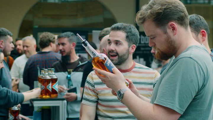 Whiskey enthusiasts examining a distinctive Jameson bottle at a busy Belfast Whiskey Week tasting event