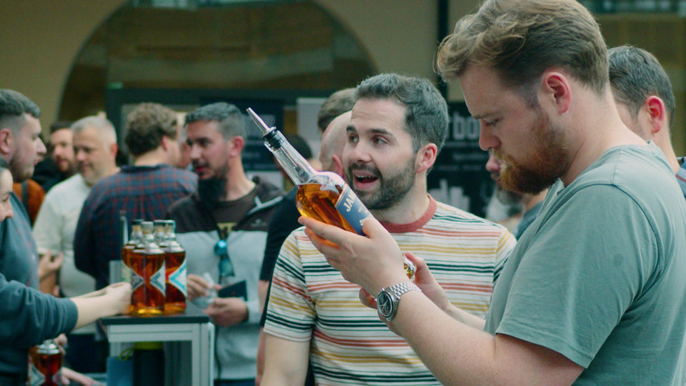 Whiskey enthusiasts examining a distinctive Jameson bottle at a busy Belfast Whiskey Week tasting event