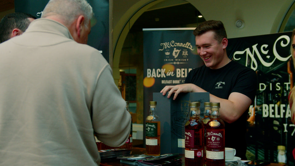 McConnell's Irish Whiskey ambassador presenting bottles to a visitor at the Belfast Whiskey Week tasting fair