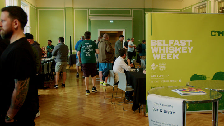 Guests mingling at a Belfast Whiskey Week event beside the festival's green branded banner
