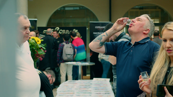 Festival-goer sampling whiskey at a Belfast Whiskey Week tasting event, with Copeland and Connacht distillery stands in the background