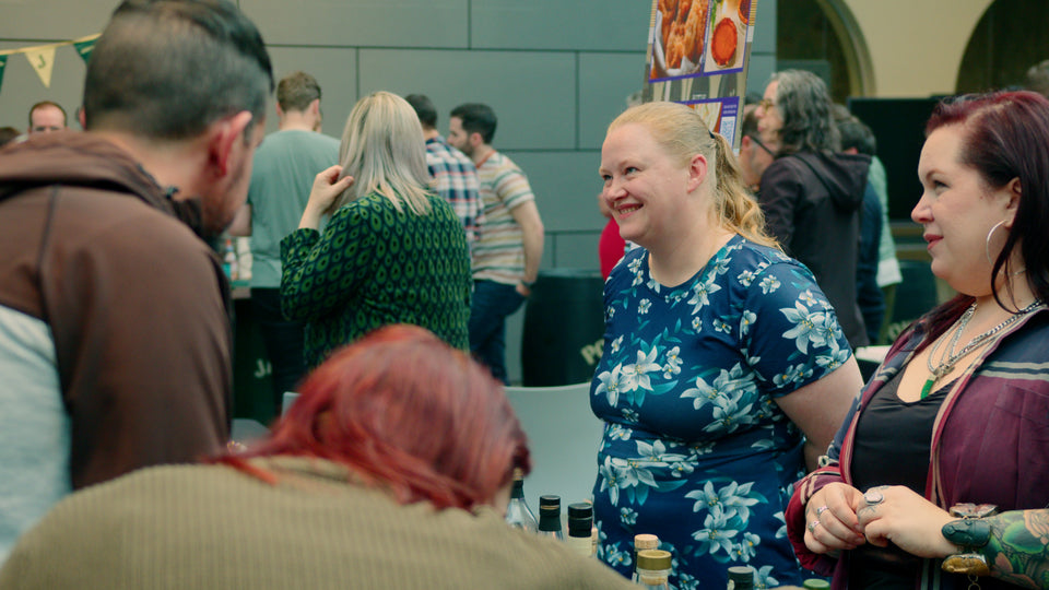 Guests smiling and socialising at a whiskey tasting stand during Belfast Whiskey Week