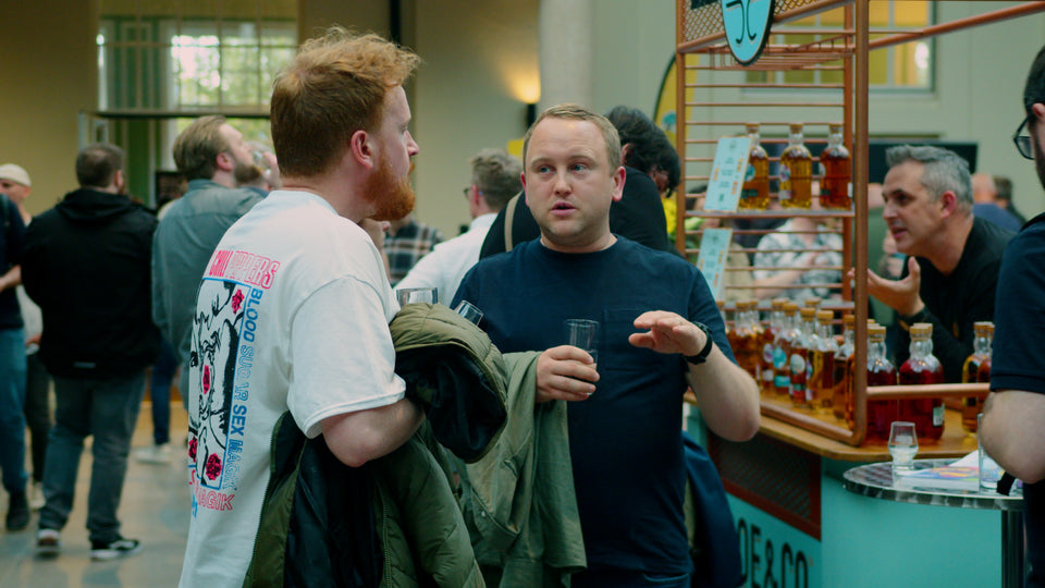 Whiskey enthusiasts chatting and tasting drams at a Belfast Whiskey Week festival stand