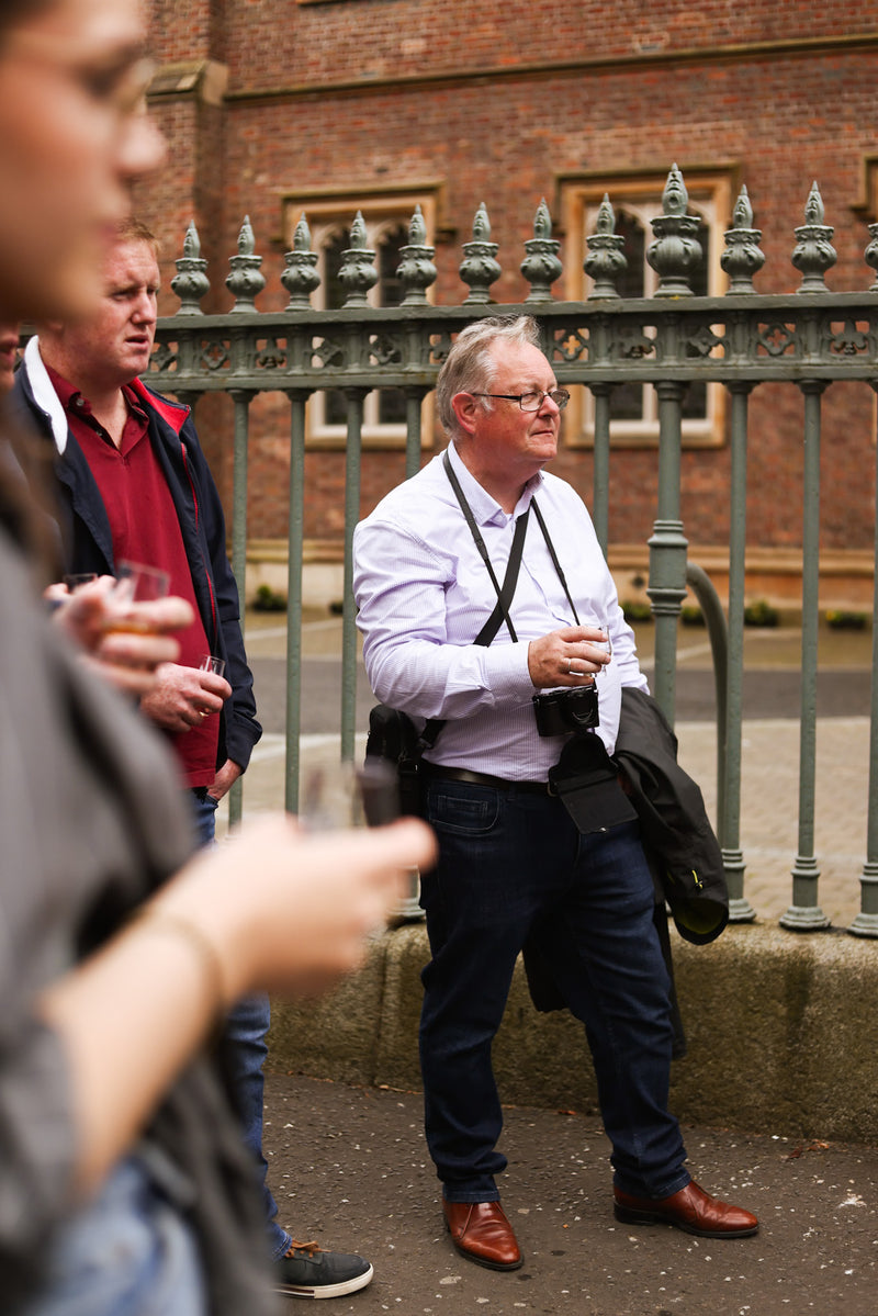 Older gentleman with camera listening attentively, guests holding drams