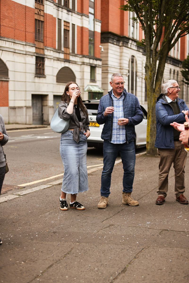 Street-side moment: woman sipping whiskey, others mid-discussion or laughing