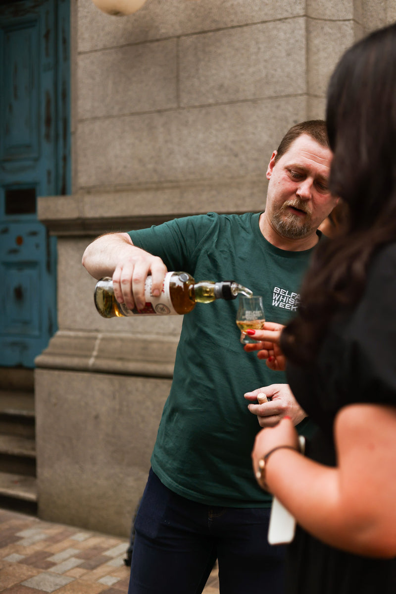Belfast Whiskey Week pouring whiskey into guest glass near granite building