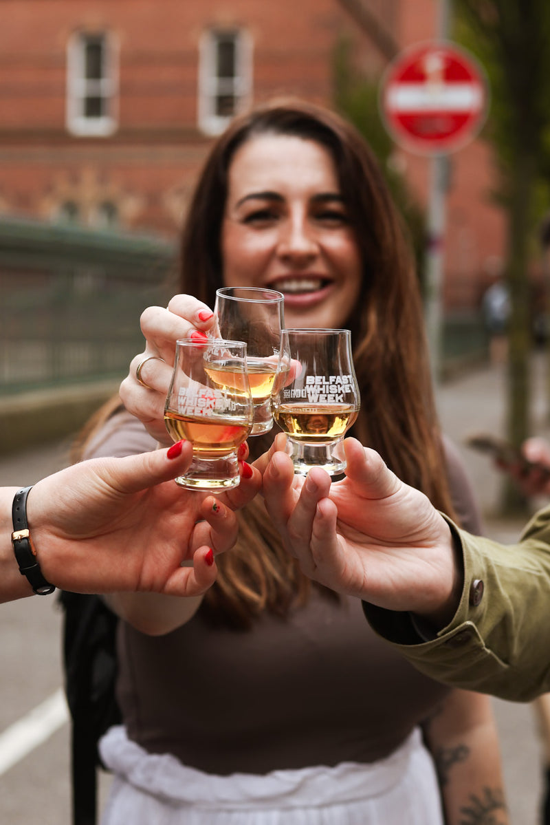 Close-up of branded Belfast Whiskey Week tasting glasses mid-toast