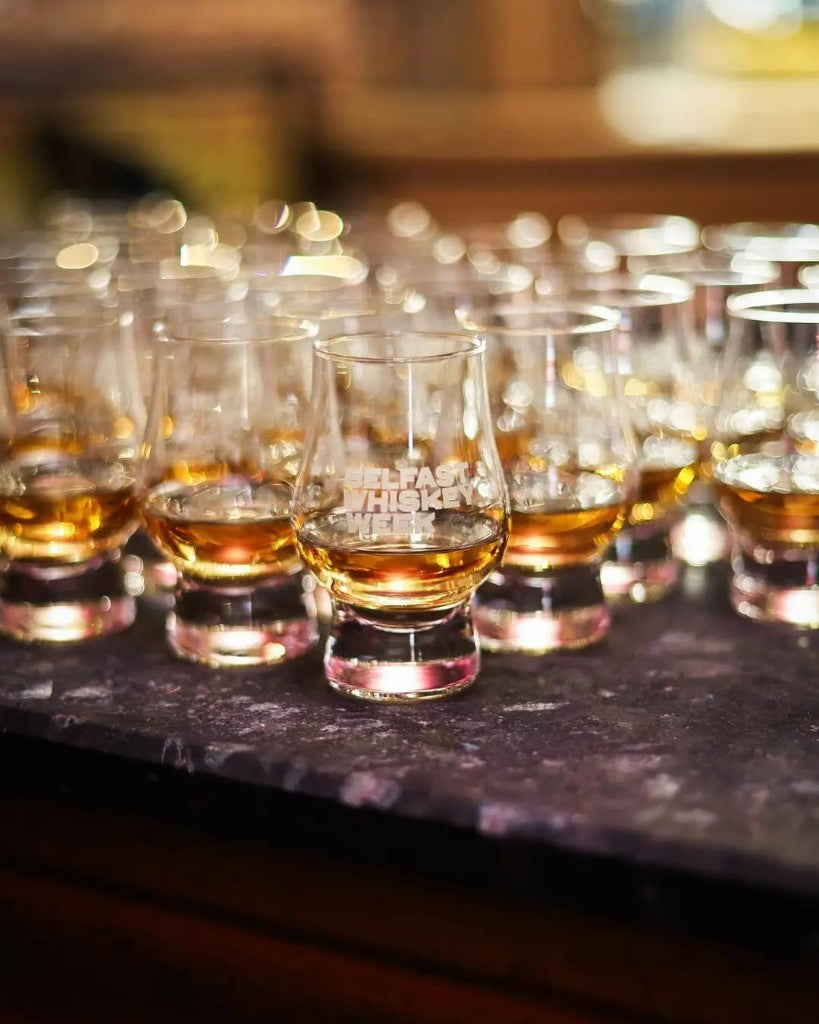 Belfast Whiskey Week branded Glencairn tasting glasses filled with amber whiskey at a festival tasting session