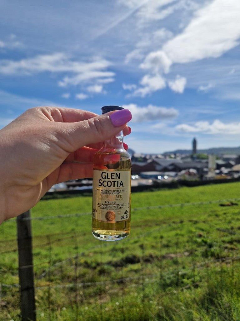 Glen Scotia Campbeltown single malt Scotch whisky miniature held up against the Campbeltown skyline