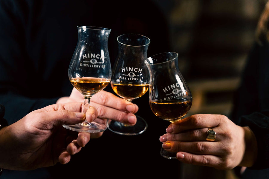 Three guests raising Hinch Distillery tulip glasses of whiskey in a toast