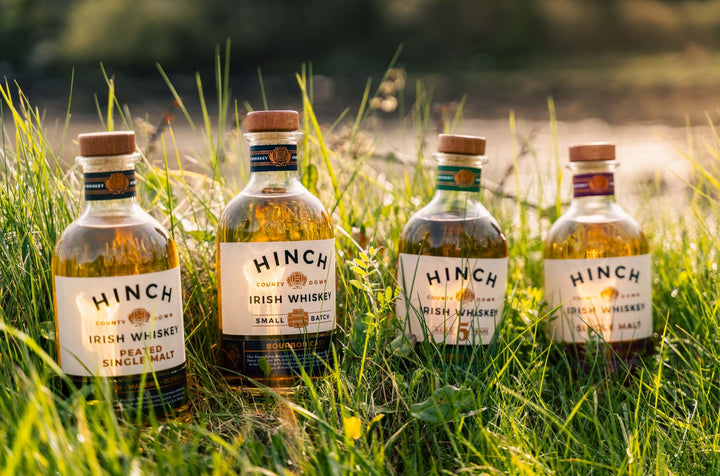 Hinch Irish whiskey range — Peated Single Malt, Small Batch, 5 Year Old and Single Malt bottles in a sunlit meadow