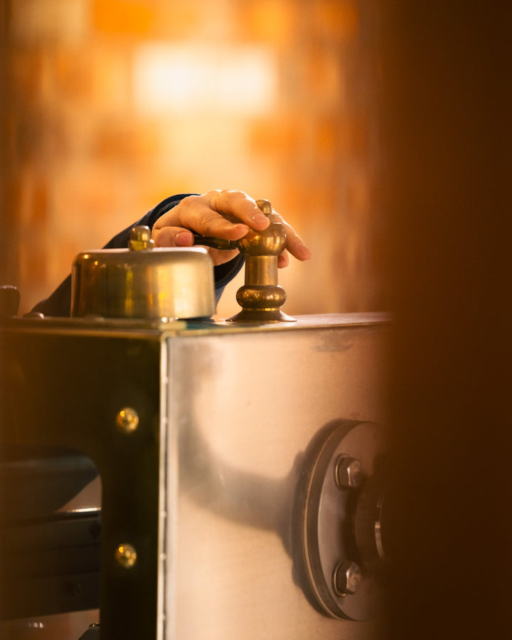 Hand on the polished brass fittings of a still at Hinch Distillery
