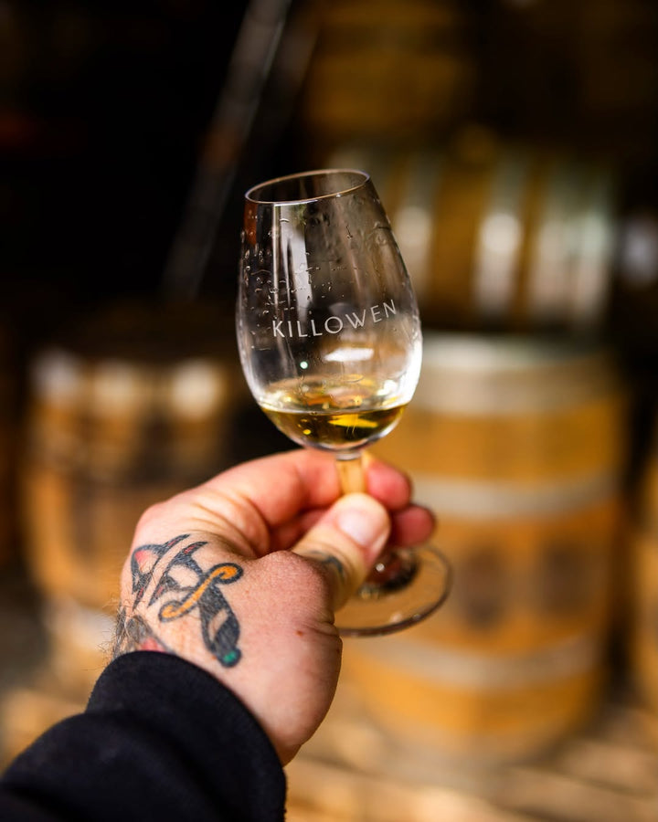 Killowen tasting glass of cask-strength whiskey held up in the barrel room