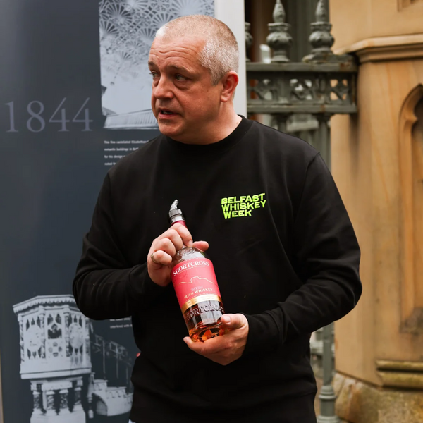 Belfast Whiskey Week guide holding a Shortcross Irish Whiskey bottle during an outdoor whiskey walking tour